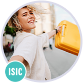 Usměvavá mladá žena si vesele vykračuje s kufrem v ruce a fotí si při tom selfie.